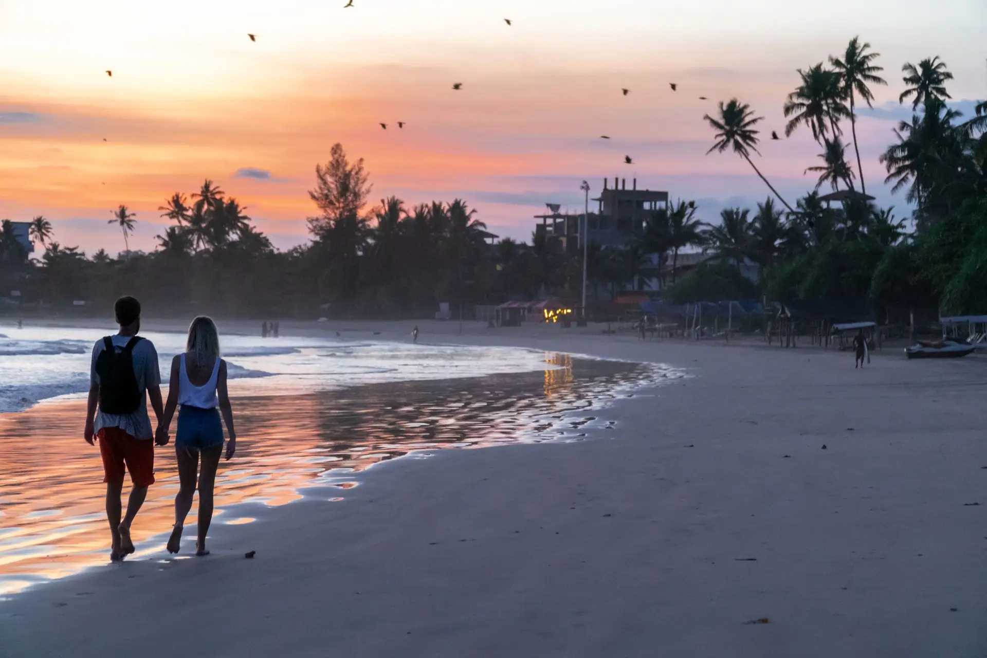 Ett par går hand i hand längs en strand på Sri Lanka i solnedgången